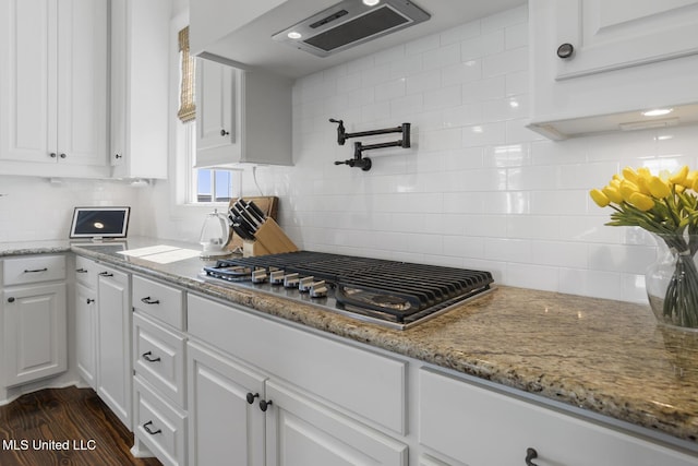 kitchen with light stone counters, stainless steel gas cooktop, decorative backsplash, white cabinets, and exhaust hood