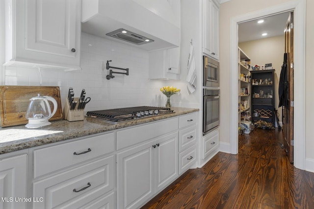 kitchen with decorative backsplash, appliances with stainless steel finishes, dark wood-style flooring, light stone countertops, and white cabinetry