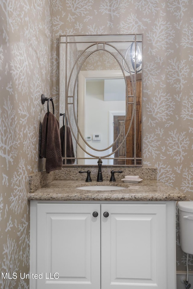 bathroom featuring toilet, vanity, and wallpapered walls