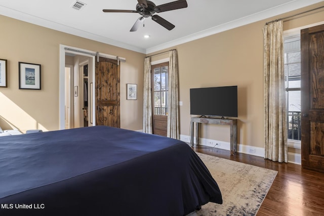 bedroom featuring a barn door, wood finished floors, visible vents, baseboards, and crown molding