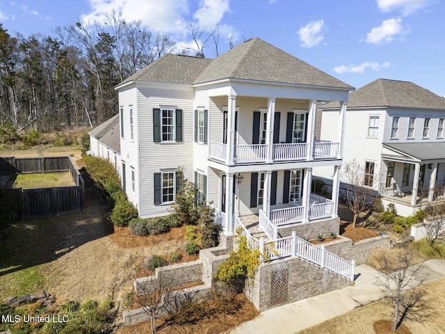 neoclassical / greek revival house featuring a balcony, covered porch, a shingled roof, fence, and stairway