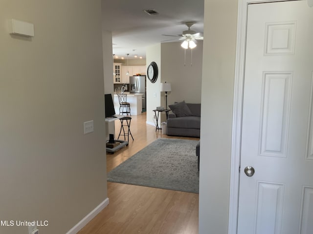 hallway with light wood-style floors, visible vents, and baseboards