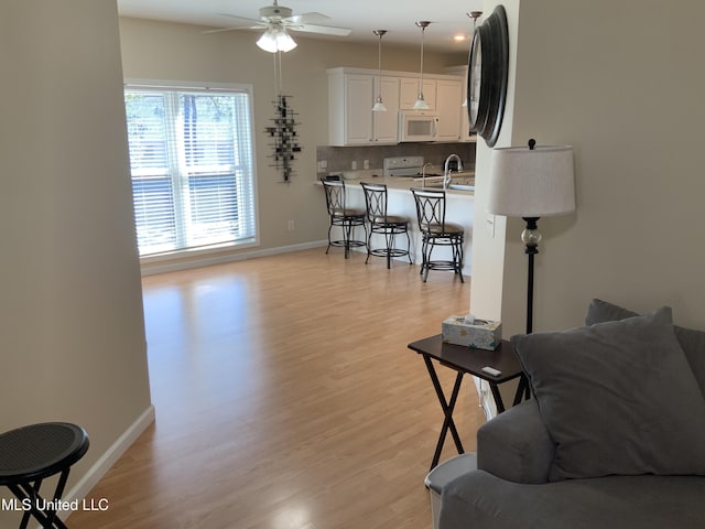 living room with light wood-style flooring, baseboards, and ceiling fan