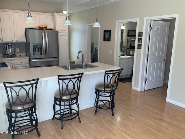 kitchen with a sink, a kitchen breakfast bar, light countertops, light wood-type flooring, and stainless steel refrigerator with ice dispenser