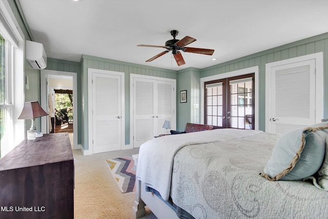 bedroom featuring french doors, ceiling fan, light colored carpet, a wall unit AC, and multiple closets