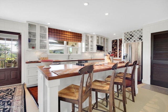 kitchen with wood counters, a center island, a breakfast bar, white cabinetry, and stainless steel appliances