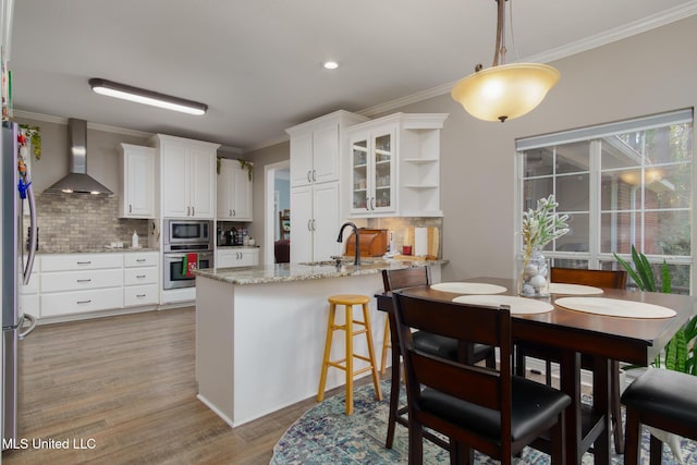 kitchen with wall chimney range hood, kitchen peninsula, decorative light fixtures, white cabinetry, and stainless steel appliances