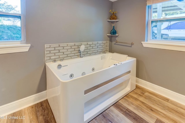 bathroom with tasteful backsplash, a tub to relax in, plenty of natural light, and hardwood / wood-style floors