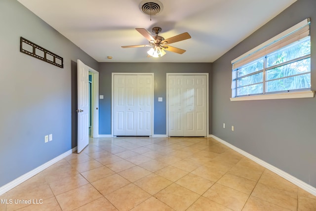 unfurnished bedroom with two closets, ceiling fan, and light tile patterned flooring