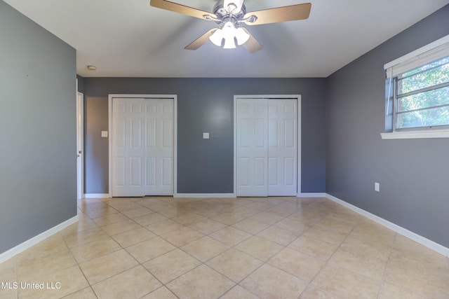 unfurnished bedroom with ceiling fan, light tile patterned flooring, and two closets