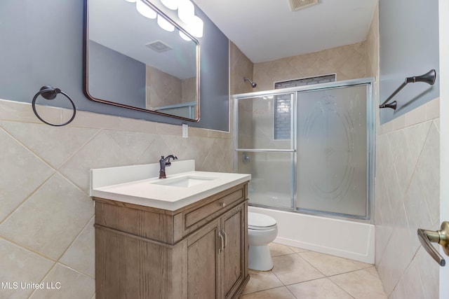 full bathroom with tile patterned flooring, bath / shower combo with glass door, toilet, vanity, and tile walls