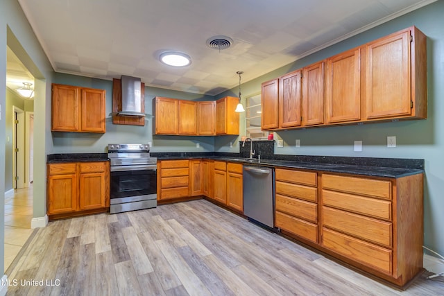 kitchen featuring wall chimney range hood, sink, hanging light fixtures, light wood-type flooring, and appliances with stainless steel finishes