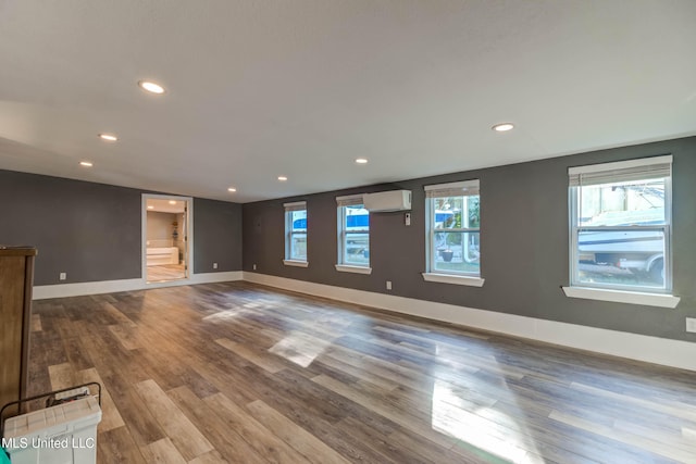 unfurnished living room featuring hardwood / wood-style floors, a healthy amount of sunlight, and a wall unit AC