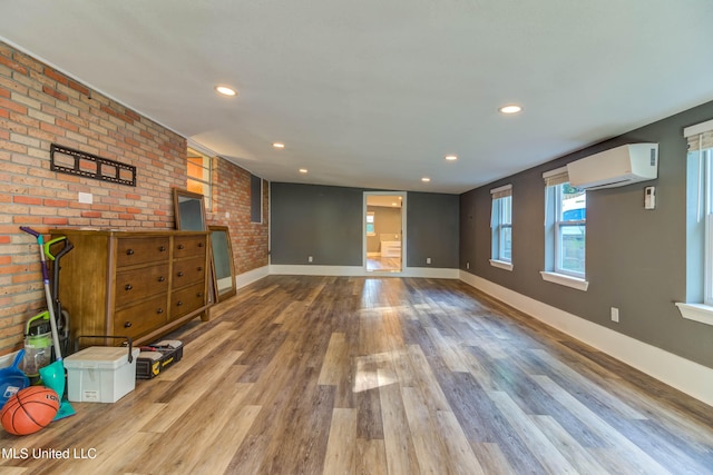 unfurnished living room featuring an AC wall unit, wood-type flooring, and brick wall