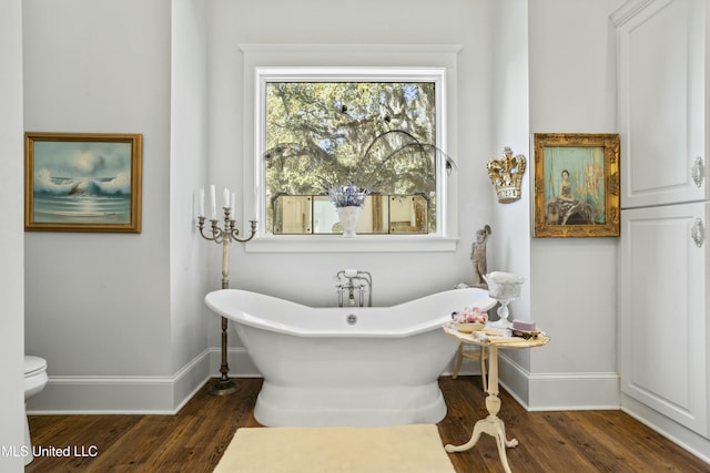 bathroom featuring a soaking tub, toilet, baseboards, and wood finished floors