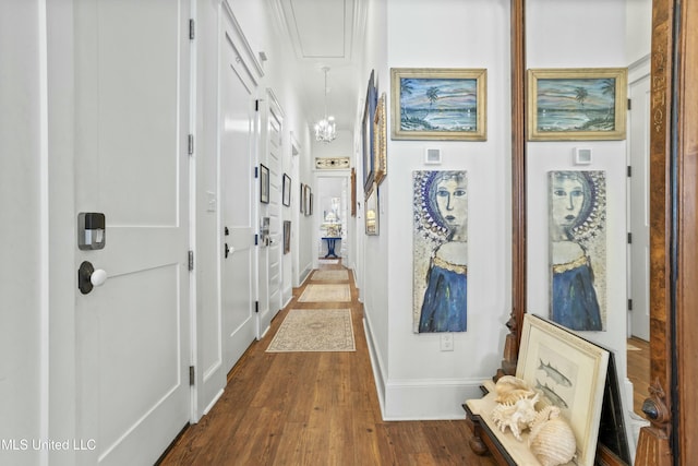 hall featuring dark wood-style flooring, baseboards, and an inviting chandelier