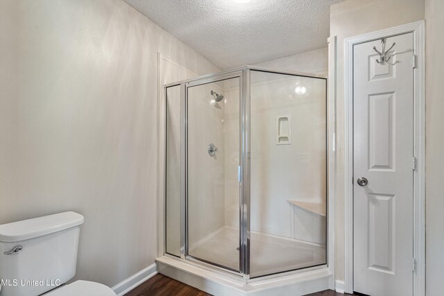 bathroom with wood-type flooring, a shower with shower door, a textured ceiling, and toilet