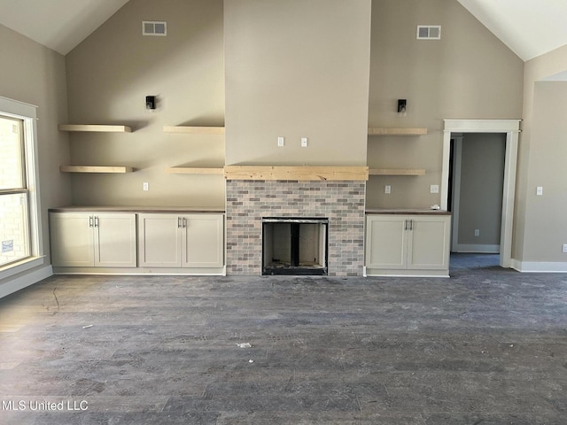 unfurnished living room featuring baseboards, a fireplace, visible vents, and high vaulted ceiling