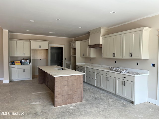 kitchen with a sink, unfinished concrete floors, a center island with sink, and ornamental molding