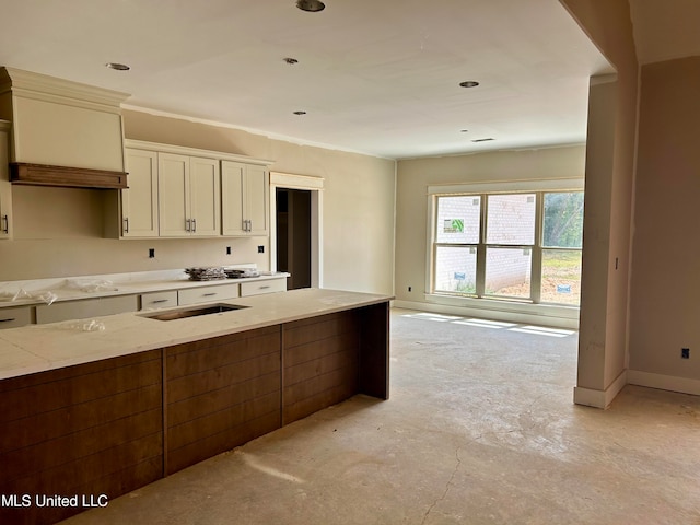 kitchen featuring light stone counters, a sink, unfinished concrete flooring, white cabinetry, and baseboards