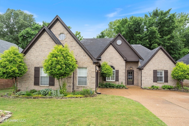 french country inspired facade with a front lawn, brick siding, and roof with shingles