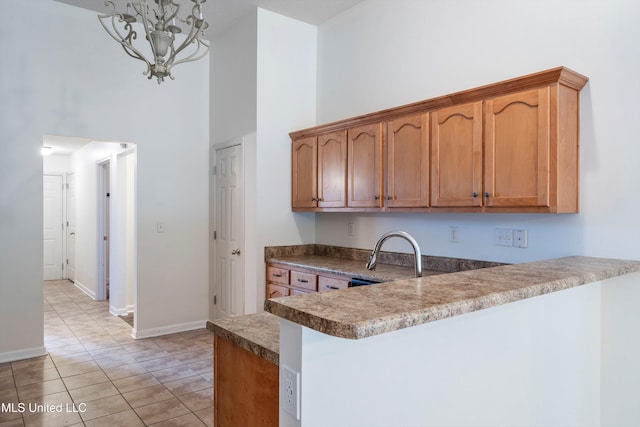 kitchen featuring a sink, a towering ceiling, a peninsula, baseboards, and a chandelier