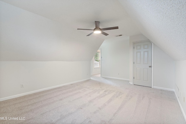 additional living space with light colored carpet, ceiling fan, a textured ceiling, vaulted ceiling, and baseboards