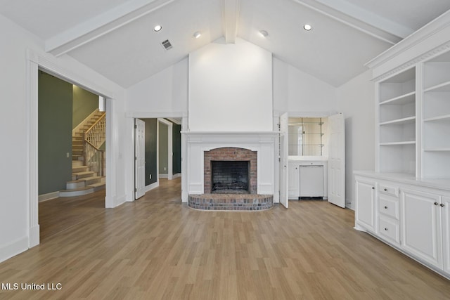 unfurnished living room with light hardwood / wood-style flooring, a fireplace, and lofted ceiling with beams