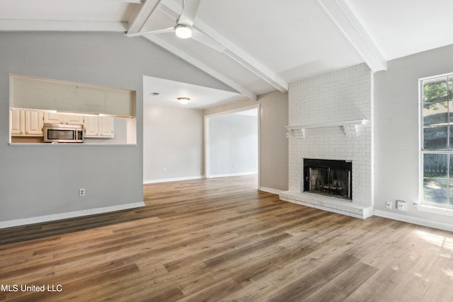 unfurnished living room featuring vaulted ceiling with beams, wood-type flooring, a fireplace, and ceiling fan