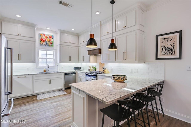 kitchen with decorative light fixtures, sink, white cabinetry, a kitchen breakfast bar, and stainless steel appliances