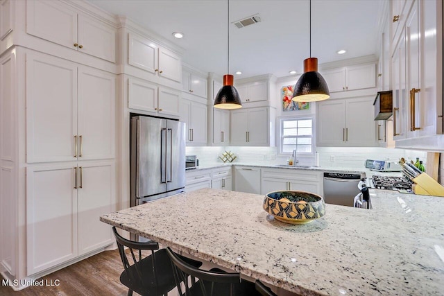 kitchen featuring white cabinets, appliances with stainless steel finishes, decorative light fixtures, sink, and light stone counters