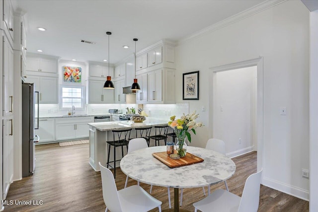 dining area with dark wood-type flooring, ornamental molding, and sink