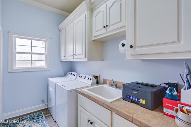 clothes washing area with washer and dryer, hardwood / wood-style floors, sink, ornamental molding, and cabinets