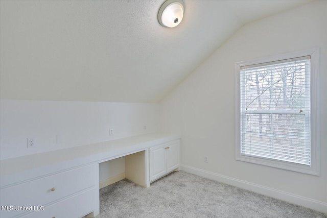 unfurnished office featuring vaulted ceiling, built in desk, and light colored carpet