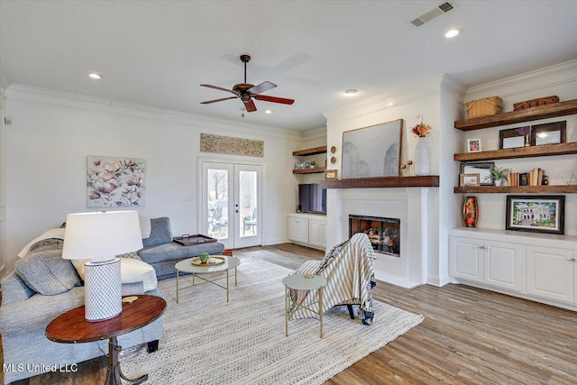 living room with a large fireplace, crown molding, light hardwood / wood-style floors, and french doors