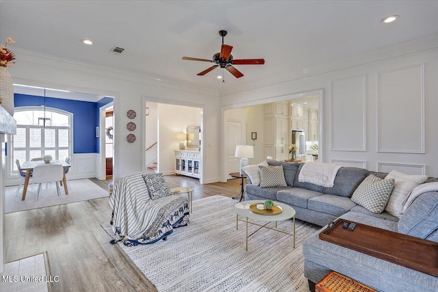 living room with ceiling fan, light wood-type flooring, and ornamental molding