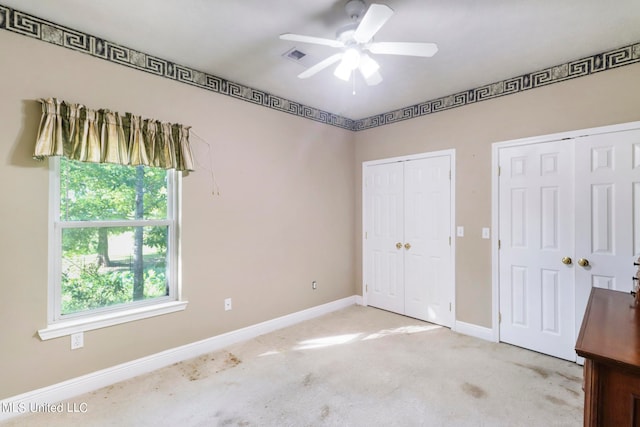 unfurnished bedroom featuring multiple windows, two closets, light colored carpet, and ceiling fan