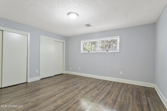 unfurnished bedroom with a textured ceiling, two closets, and dark wood-type flooring