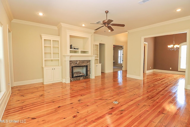 unfurnished living room with crown molding, built in features, light hardwood / wood-style floors, and ceiling fan with notable chandelier