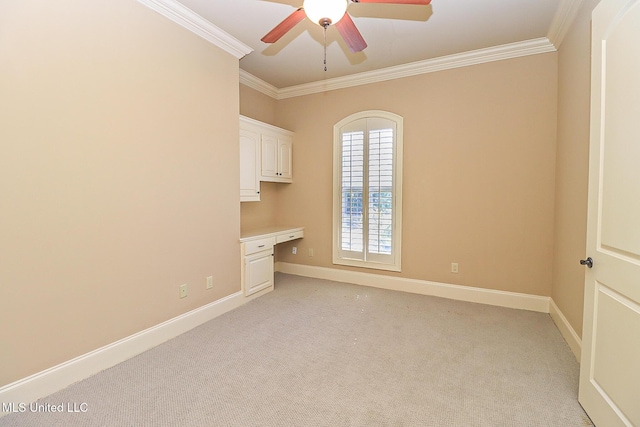 spare room featuring ceiling fan, light colored carpet, crown molding, and built in desk