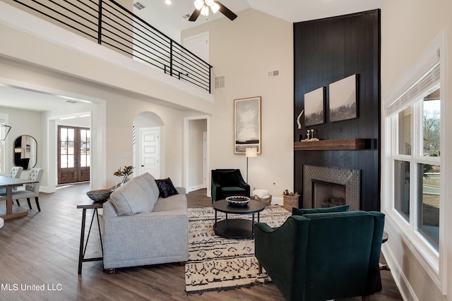 living room with a large fireplace, ceiling fan, visible vents, baseboards, and arched walkways