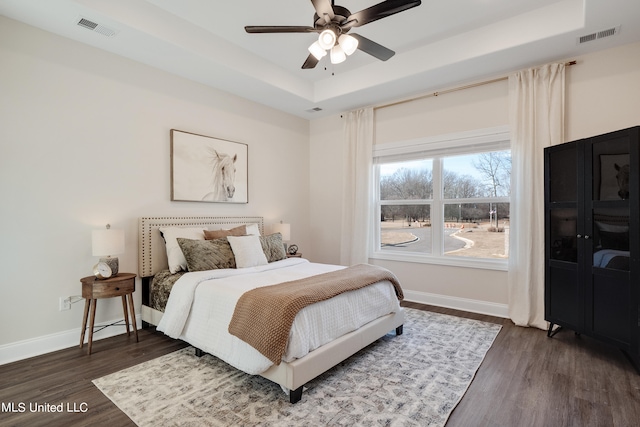 bedroom with ceiling fan, a raised ceiling, and dark hardwood / wood-style floors