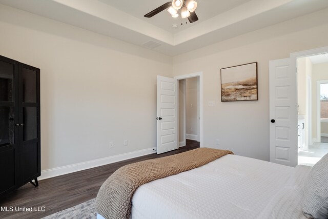 bedroom with dark hardwood / wood-style flooring, a tray ceiling, and ceiling fan