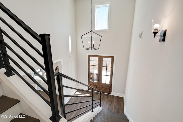 staircase with hardwood / wood-style floors, french doors, and a notable chandelier