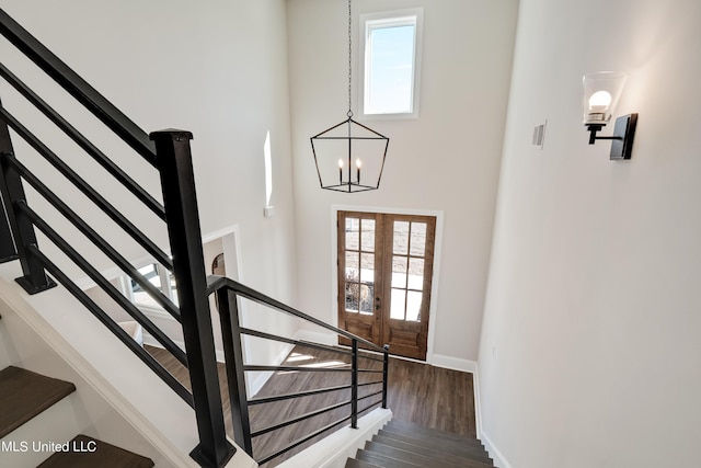 stairs featuring french doors, baseboards, an inviting chandelier, a towering ceiling, and wood finished floors