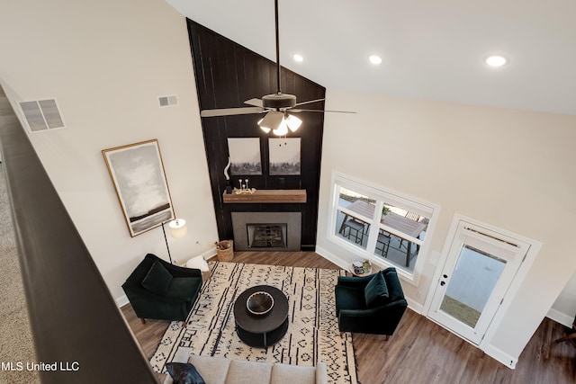 living room featuring a fireplace, high vaulted ceiling, visible vents, baseboards, and wood finished floors