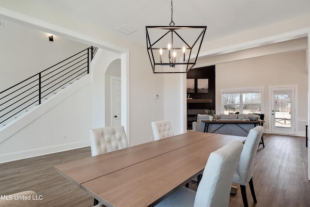dining room featuring wood finished floors, arched walkways, a chandelier, baseboards, and stairway