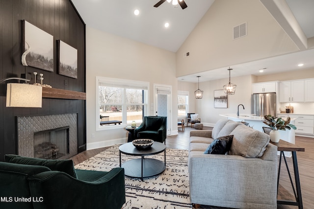 living room with hardwood / wood-style flooring, high vaulted ceiling, a large fireplace, and ceiling fan