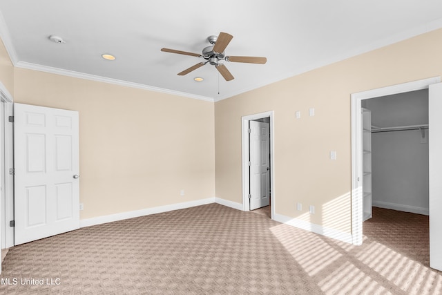 unfurnished bedroom featuring a spacious closet, carpet, a closet, ceiling fan, and crown molding