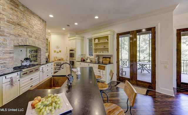 kitchen featuring stainless steel appliances, open shelves, dark countertops, a sink, and crown molding